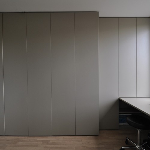 Onze klant wou een bureau laten inrichten dat vooral praktisch was, maar ook met een stijlvolle en strakke uitstraling. Wij maakten een wandkast over de volledige breedte van de muur. Om voldoende licht te behouden werd de maatkast gedeeltelijk minder diep gemaakt. Onder het bureau werd ook een ladekast geïntegreerd. Alle draaideuren werden voorzien van het tip-on systeem, waarbij je de deur opent met een zachte druk.  Kast-ID Asse