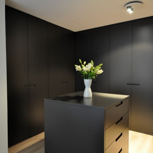 Ce dressing a été intégré dans la chambre à coucher et nous avons dès lors opté pour le même style sobre pour les armoires. Les faces extérieures ont été habillées d’anthracite, tandis
