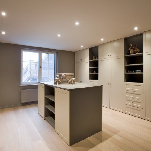 Dans cette ancienne chambre à coucher a été conçu un dressing complet en style ‘cottage’. L’îlot crée un équilibre entre les parois des deux séries d’armoires.  Kast-ID Gent