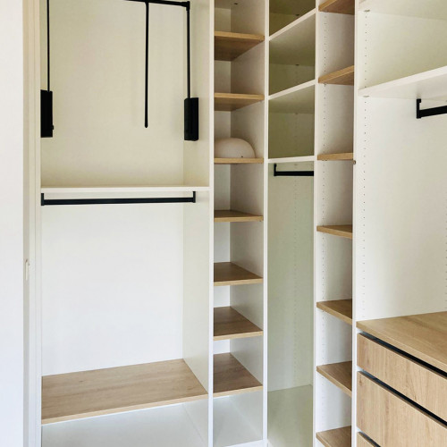 Voor deze klant realiseerden we een mooie open dressing. De kasten werden uitgevoerd in wit, met leggers en lades in decor Riverside Oak als speelse toets. Om het geheel af te werken kozen we voor mat zwart gelakt garderobestangen. De maatkasten werden netjes onder de schuine wand geplaatst.