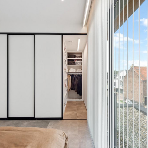 Voor deze klanten mochten we maatkasten voorzien in de slaapkamer. Achter de schuifdeuren maakten we links een ruime kleerkast , voorzien van hangroedes, een kledinglift en lades. Rechts bevond zich een kleine inham naast de liftschacht. Deze werd handig omgetoverd tot kleine inloopkast . Het zwarte frame van de schuifdeuren contrasteert mooi met de witte slaapkamer.